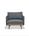 The Pensive Lounge Chair | Fabric by Wooden Stories features blue-gray upholstery, wooden legs, and elegant Danish-inspired lines in a simple boxy design, shown against a plain white background.