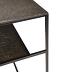 A close-up of Ethnicrafts Pentagon Console - Whiskey, featuring a black metal frame and two textured dark brown shelves crafted with mineral powders and natural color pigments, set against a white background.