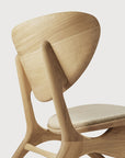 A close-up of the Ethnicraft Eye Lounge Chair - Oak, showcasing its smooth curved lines, rounded backrest, and light beige upholstered seat that accentuates the European oaks wood grain and fine craftsmanship.