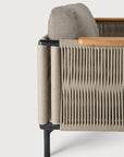 Close-up side view of the Ethnicraft Corbey Outdoor Sofa, showcasing tightly woven beige rope, a black metal frame, wooden armrest accents, and a light gray cushion—an ideal addition to your outdoor space.