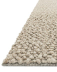A close-up of the Loloi Quarry Rug - Oatmeal shows its chunky-loop, hand-knotted wool texture with a pebble-like surface in calming beige neutrals, displayed against a white background.