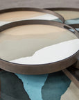 The Sand Wabi Sabi Glass Tray - Round / Small by Ethnicraft features an abstract, pastel-toned design and a dark metal rim, evoking the tranquil beauty of the Blue Ridge Mountains.