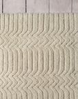 A close-up of the Savannah Rug - Natural by Armadillo&Co, featuring a cream-colored, textured wool and cotton blend with a zigzag pattern, displayed on a light wooden floor.