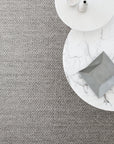 Two round tables, one white marble and one white, overlap on Armadillo&Cos Sherpa Weave Rug in Pumice. On the tables are a gray envelope-shaped object, a small vase, and a ceramic bowl.