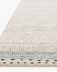 Close-up of the Loloi Sloane Rug - Mist, a hand-woven piece in subtle gray and beige tones. Its edge highlights small, evenly spaced black dots on a light background, adding a contemporary bohemian accent.