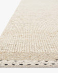 A close-up of the Sloane Rug - Oatmeal by Loloi shows its off-white, hand-woven texture, detailed edge stitching, and a soft, subtle pattern.