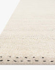 A close-up of the Sloane Rug - Sky by Loloi showcases its cream hue and subtle black edging, hand-woven with a contemporary bohemian flair against a white background.