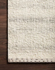 A close-up of the Loloi Sloane Rug - Sky, showcasing its cream and gray stripes and chunky texture, displayed on a dark hardwood floor for a contemporary bohemian look viewed from above.