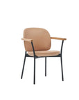 The Solace Dining Armchair by Wooden Stories features a modern design with beige leather cushioned seat and backrest, black metal legs, and light wooden armrests, displayed against a plain white background.