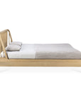 The Ethnicraft Spindle Bed - Oak features a slatted headboard and European oak construction, shown from the side with light gray and beige bedding and two matching pillows, set against a white background.