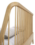 Close-up of the Ethnicraft Spindle Bed - Oak, crafted from European oak with vertical slats and a curved headboard, shown with light gray bedding neatly arranged.