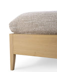 Close-up of Ethnicraft’s Spindle Bed - Oak, featuring angled legs and showcasing the clean lines and European oak grain, topped with a thick beige and white textured blanket.
