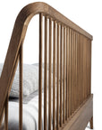Close-up of Ethnicraft’s Spindle Bed - Teak, showcasing vertical slats and a curved headboard crafted from reclaimed FSC-certified teak. A gray knit pillow and white bedding are partially visible against a white background.