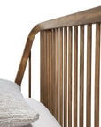 Close-up of the Ethnicraft Spindle Bed - Teak, featuring vertical slats and a curved corner. A textured light gray pillow and white bedding appear in the lower left against a plain white background.