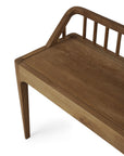 A partial view of the Ethnicraft Spindle Bench - Natural Teak shows its smooth seat, angled legs, and a backrest with vertical slats and a rounded top rail, all crafted from natural teak.