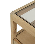 Close-up of the Spindle Nightstand - Oak by Ethnicraft, showcasing its solid oak frame and glass top insert, with a focus on the light wood grain and robust build.