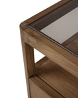 Close-up of the Ethnicraft Spindle Nightstand - Teak, crafted from FSC-certified teak with a smooth-edged glass top and lower shelf, combining sturdy construction with elegant design.