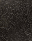 Close-up of the dark, cracked, and textured surface of the Stability Coffee Table - Umber by Ethnicraft, displaying irregular lines reminiscent of dried earth and showcasing refined European-inspired tabletop finishes.