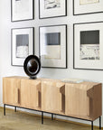 The Ethnicraft Stairs Sideboard - 4 door, featuring sculpted oak doors, stands against a white wall topped with a round black bowl and a book. Above it, six abstract black-and-white artworks are arranged in two rows.