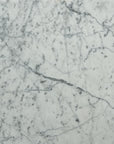 Material Swatches by Natadora + Tolv feature a white marble surface with gray and black veining, natural speckles, and a smooth finish—highlighting elegant organic shapes and intersecting lines in their collection.