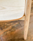Close-up of the SOBU Sven Dining Chair - White Ash, crafted from solid ash with curved edges and visible grain detail on the seat and leg. The durable lacquer finish contrasts beautifully with a rustic wooden floor.