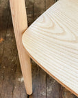 Close-up of the SOBU Sven Dining Chair - White Ash, highlighting its solid ash seat, visible wood grain, and durable lacquer finish, set atop a rustic dark wooden floor.