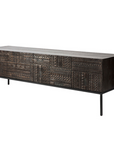 The Ethnicraft Tabwa TV Cupboard - 63 is a long, rectangular dark wood piece featuring intricate, linear geometric carvings on slim black metal legs, inspired by Tabwa culture and shown against a white background.