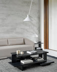 A modern living room with a light beige sofa, an Ethnicraft Teak Abstract Coffee Table featuring books and decor, a white table lamp on a side table, a gray rug, and a white pendant light set against a textured gray wall.