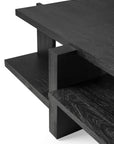 A close-up of the Ethnicraft Teak Abstract Coffee Table, a modern black wooden piece inspired by de Stijl, with clean lines and two staggered rectangular shelves supported by thick vertical blocks.