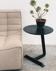 A potted succulent rests on the Teena Side Table - Black Ash by SOBU, next to a beige tufted sofa on a concrete floor against a white wall.