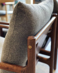 Close-up of the SOBU Viking Lounge Chair - Walnut, showing its solid walnut frame with rounded corners and a grey high-density foam cushion. Another chair appears blurred in the background of a naturally lit indoor space.
