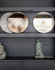 A dark wood Ethnicraft shelving unit displays two small, round White Slice Wooden Trays by Ethnicraft, a rectangular geometric artwork, and two small bronze robed figure sculptures on the lower shelf.