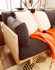 The SOBU Woody Sofa in white ash and charcoal features dark gray cushions, two white pillows with black tassels, and an orange blanket on a striped rug; its machine washable covers make care easy for any bright living room.