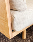 Close-up of the SOBU Woody Sofa SAMPLE_(DZ): modern beige upholstery, solid ash wood frame, textured fabric cushion with high-density foam, and a glimpse of a woven rug on the floor.