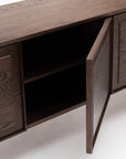 A close-up of the Yorke Sideboard by Wooden Stories, crafted from solid oak in a dark wood finish, shows one paneled door open to reveal an empty interior shelf. The sideboard is set against a white background.