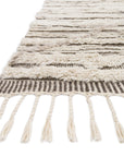 A close-up of Loloi’s Khalid Rug in Ivory/Taupe reveals thick, varied patterns and fringed tassels. Hand-knotted from 100% wool, this Moroccan-style rug looks plush and soft against a white background.