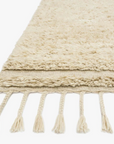 A close-up of the Loloi Hygge Rug in Oatmeal/Sand, hand-loomed from 100% wool with braided tassels, shown against a white background.