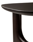 Close-up of the Ethnicraft Flow Side Table, highlighting its dark wooden finish, rounded tabletop edge, and thick, curved leg with smooth, polished surfaces.