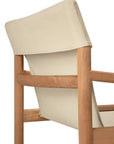 A close-up of the Safari Lounge Chair by Ethnicraft, featuring a light wood frame and beige fabric backrest, is shown from an angle behind and to the side—an embodiment of the brand’s timeless elegance.