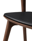 Close-up of the Ethnicraft Bok Dining Chair - Teak Brown, featuring solid teak construction, a triangular black leather seat cushion, and angled legs that highlight its smooth, minimalist design and craftsmanship.