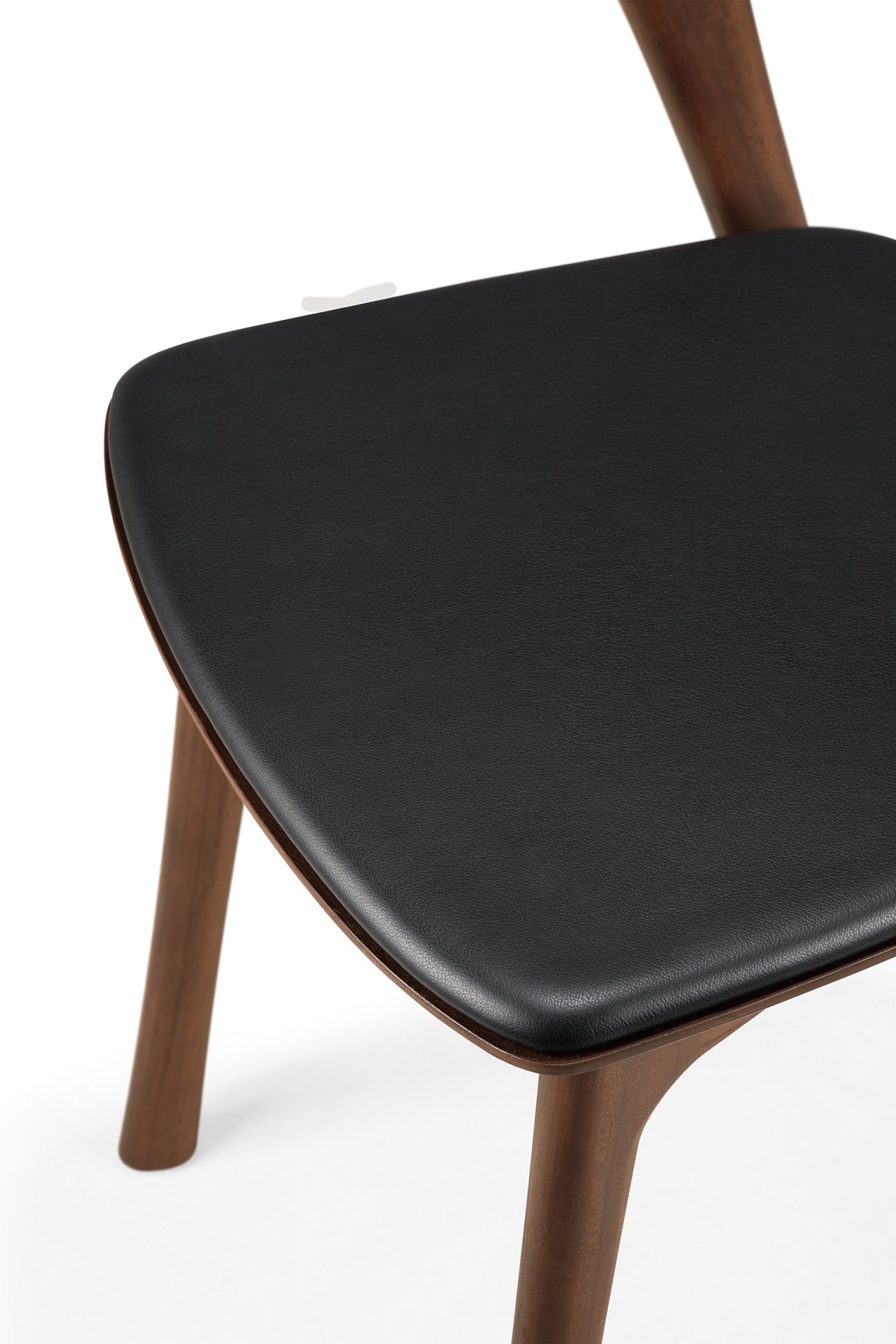 A close-up of the Ethnicraft Bok Dining Chair - Teak Brown, featuring solid teak legs and a black leather cushioned seat, set against a white background.