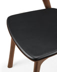 A close-up of the Ethnicraft Bok Dining Chair - Teak Brown, featuring solid teak legs and a black leather cushioned seat, set against a white background.