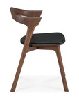 The Ethnicraft Bok Dining Chair - Teak Brown features a curved backrest and black leather seat cushion, crafted from solid teak, shown in profile against a white background.
