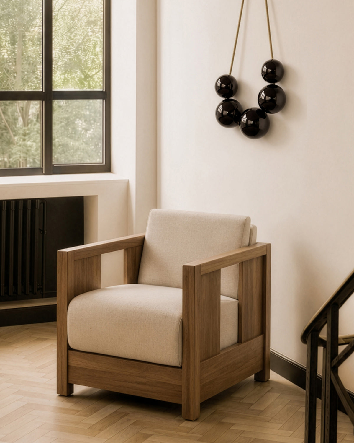 The Roan Lounge Chair | Flax by Ethnicraft, with a wooden frame and beige cushions, sits in a bright room featuring large windows, light wood floors, and wall art with black hanging spheres.