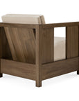 A modern armchair with a solid teak frame and flax-colored cushioned seat and backrest, viewed from the back and side to highlight its angled support and open side panels—this Roan Lounge Chair | Flax by Ethnicraft blends timeless design with the lasting beauty of solid wood craftsmanship.