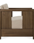Side view of the Roan Lounge Chair | Flax by Ethnicraft, a modern armchair featuring a solid teak wooden frame and a beige upholstered seat and backrest. The chair showcases clean, straight lines and an open rectangular cutout in the wooden arm panel.
