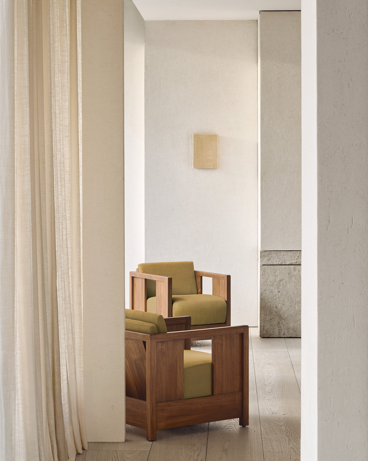 Minimalist room with neutral tones, featuring the Ethnicraft Roan Lounge Chair in Amber placed near sheer beige curtains. Light wood flooring and simple, textured walls complete the calm, modern aesthetic.