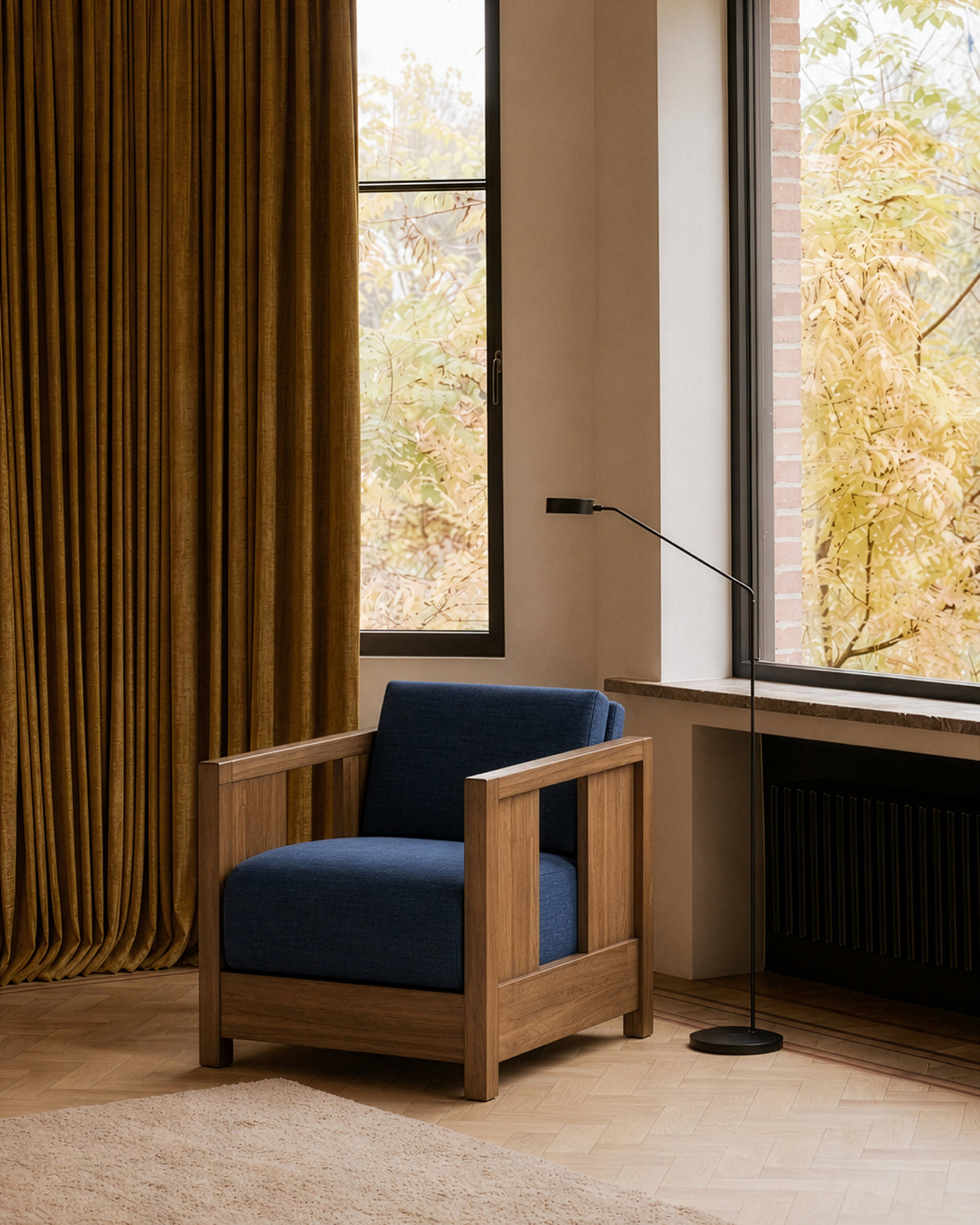 A modern Ethnicraft Roan Lounge Chair | Ink featuring deep navy cushions sits by large windows, golden curtains, and a black floor lamp in a cozy, minimalist room with light wood floors and autumn foliage visible outside.