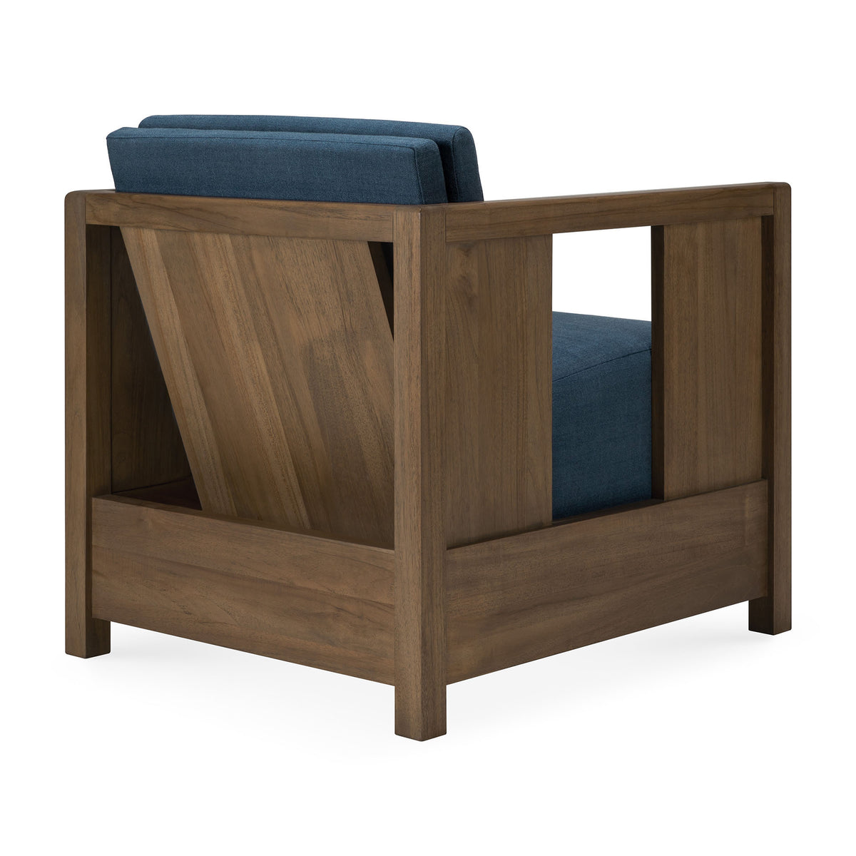 A modern, vintage-inspired Roan Lounge Chair | Ink by Ethnicraft, featuring a wooden frame and blue upholstered cushions, is shown from a rear-side angle. The back displays an angled wood panel for support, characteristic of the Roan Lounge Chair’s distinctive design.