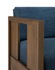 A close-up of the Ethnicraft Roan Lounge Chair | Ink, a modern wooden armchair with ink blue upholstered cushions and backrest, featuring rectangular wooden armrests and clean, minimalist lines inspired by vintage design.